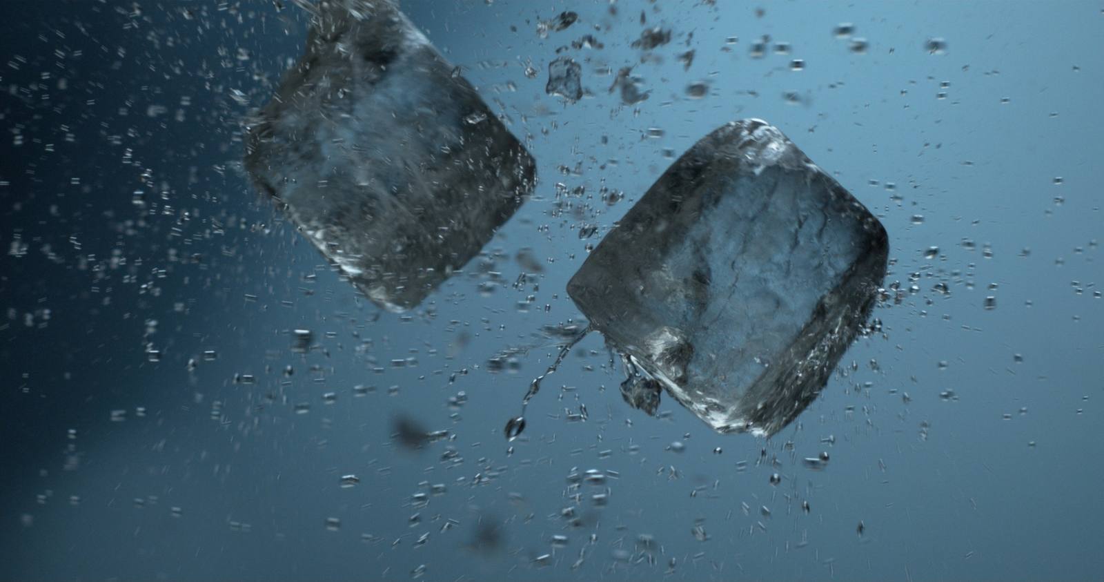 Twee ijsblokjes die in slowmotion door het water tuimelen, omringd door luchtbellen tegen een blauwe achtergrond.