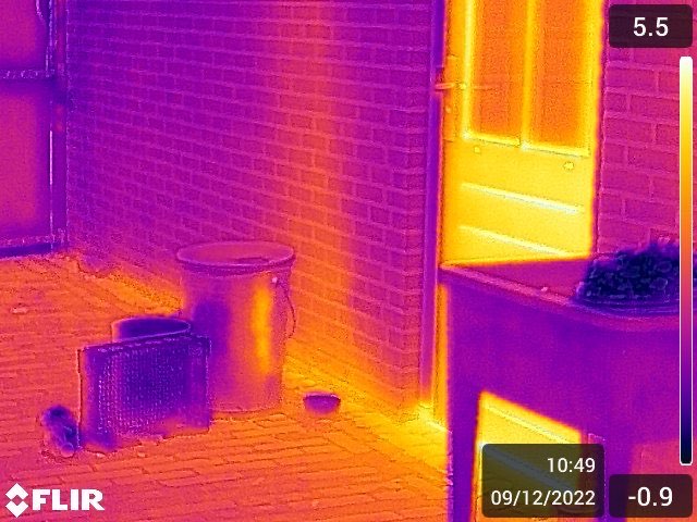 Warmtebeeldopname van een gevel en deur, waarbij warmteverlies rond het kozijn oplicht in geel en oranje.